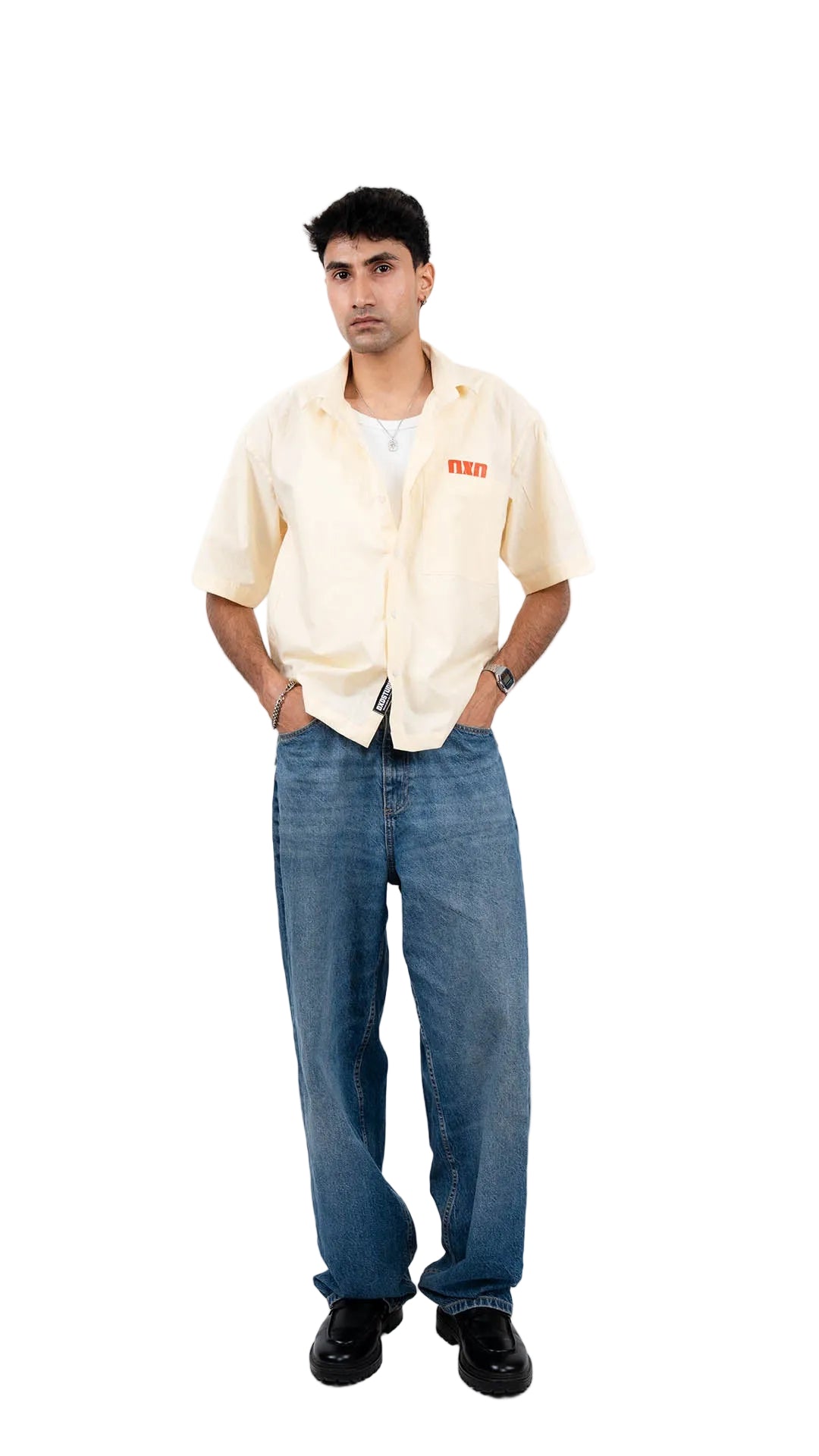 Person wearing a beige shirt with a brand logo and blue jeans on a white background